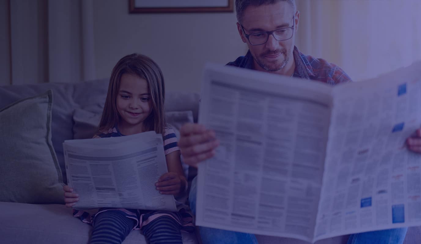 A man and his young daughter sat on the sofa, each reading a newspaper