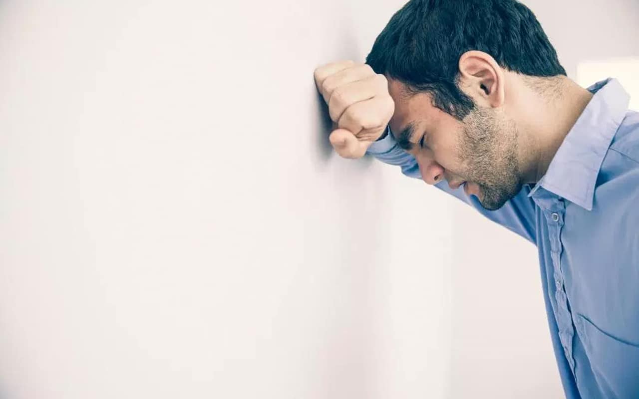 A man resting his head on the wall in frustration