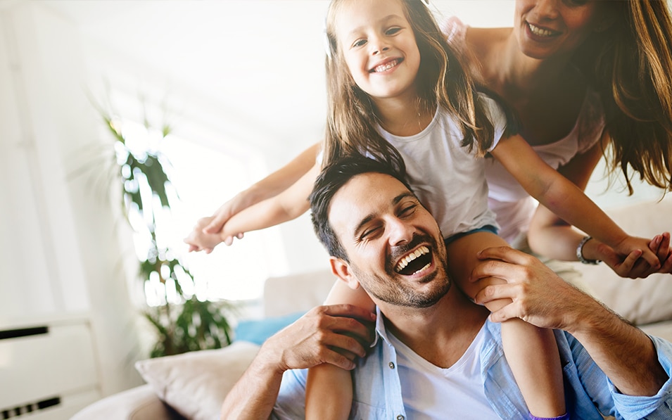 Two parents and their young daughter laughing in their home